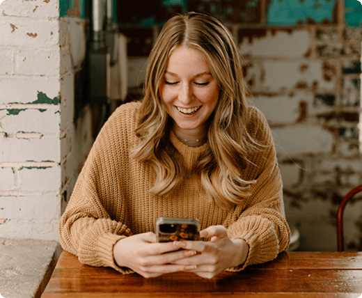 a_young_woman_is_smiling_while_looking_at_her_phone