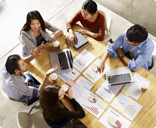 five_people_are_discussing_around_a_table_with_laptops_and_charts